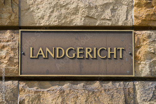German courthouse signage on brass plaque. The word “Landgericht” engraved on a golden sign mounted on a coarse stone wall.