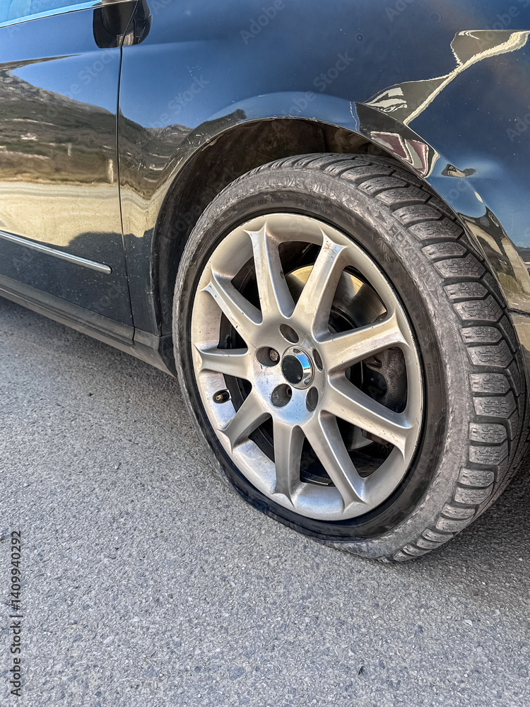 Flat front tire on a black car parked on a city street. Close-up of the deflated wheel. Suitable for illustrating car breakdowns, auto repair, road accidents, and urban vehicle issues. Flat front tire on a black car parked on a city street. Close-up of the deflated wheel. Suitable for illustrating car breakdowns, auto repair, road accidents, and urban vehicle issues.