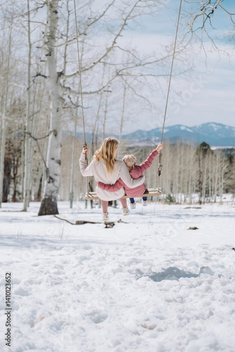 mother and daughter on a swing in a the snowy mountains