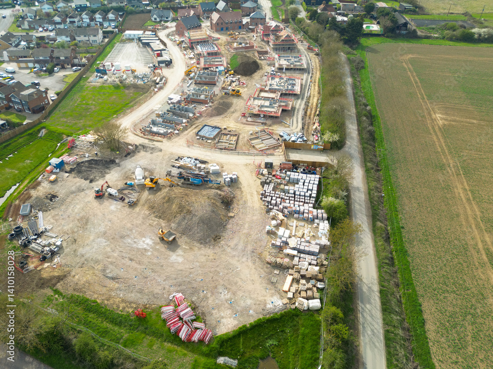 Drone high altitude view of an expansive new housing development project in rural East Anglia. Homes seen in various stages of construction, the old village is on the left.