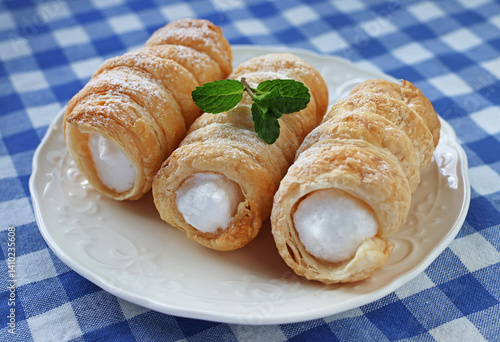 Puff pastry tubes with white cream on a white plate decorated with mint leaves, close-up