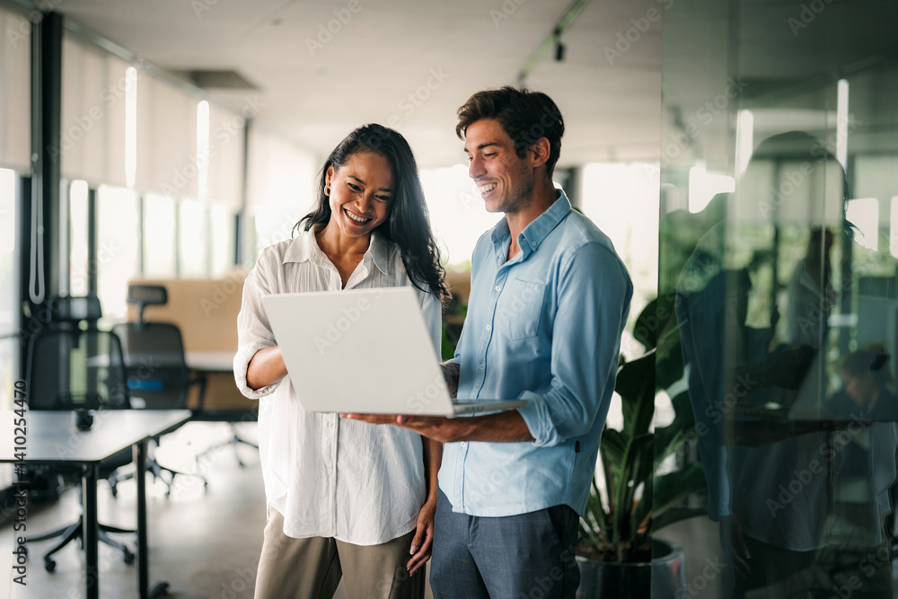 Diverse team of two business people working talking using tablet tech walking in corporate office.