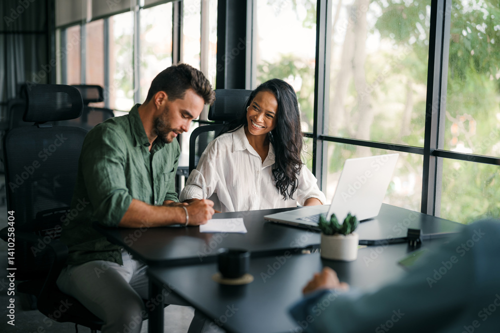Multiracial colleagues discussing startup project and smiling during workday in office interior