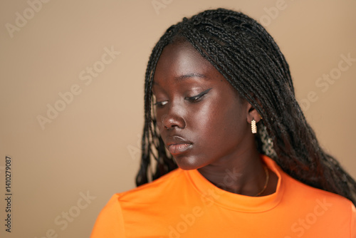 Young black woman wearing orange shirt and braids posing in studio