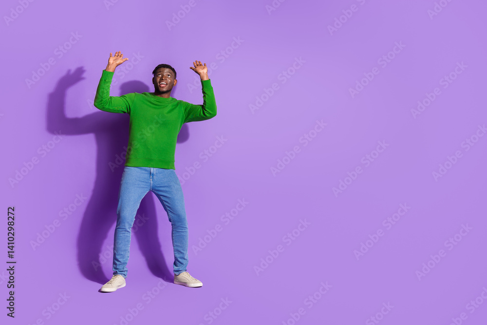 Happy young man in vibrant green pullover and denim jeans joyfully posing against solid purple studio background Happy young man in vibrant green pullover and denim jeans joyfully posing against solid purple studio background