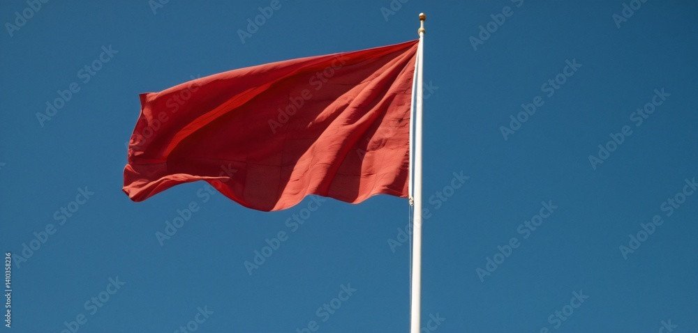 A vibrant red flag fluttering in the wind, captured in mid-motion against a clear blue sky. The fabric has a silky texture, with dynamic folds and waves that showcase the strength of the wind.