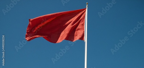 Obraz na płótnie A vibrant red flag fluttering in the wind, captured in mid-motion against a clear blue sky. The fabric has a silky texture, with dynamic folds and waves that showcase the strength of the wind. w salonie