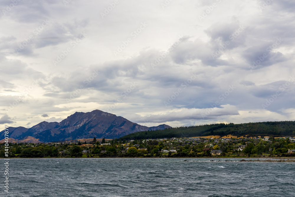 Lake Wanaka, a summer cloudy afternoon with a mountain range and the town of Wanaka on the shore. South Island, New Zealand