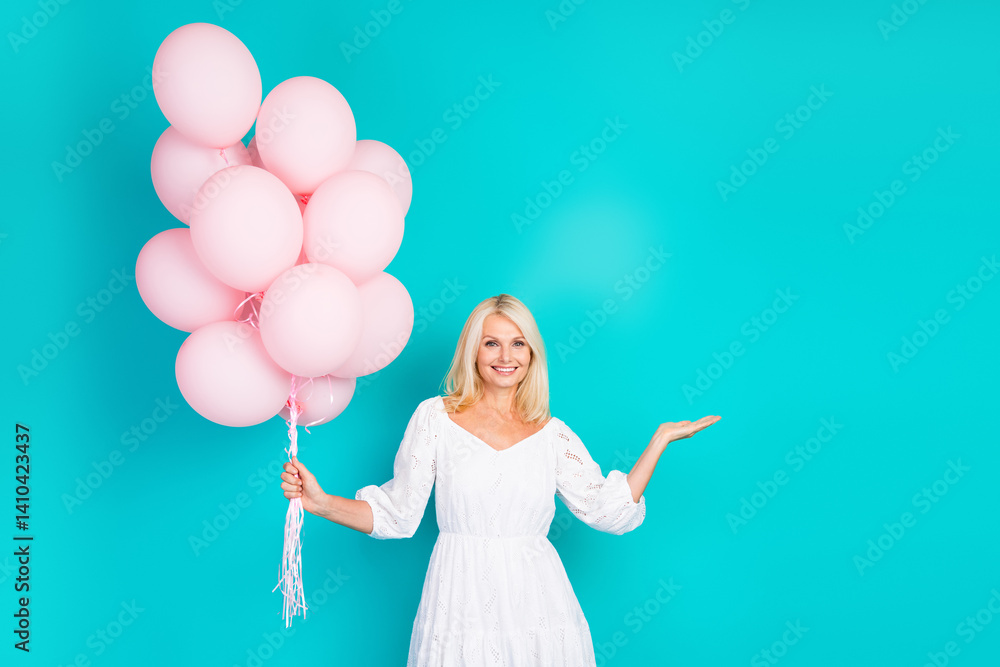 Naklejka premium Charming middle aged woman holding pink balloons and gesturing against a turquoise background, celebrating with elegance and grace