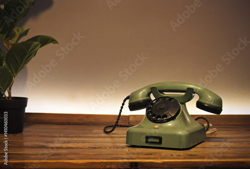 Old style cable telephone. Green vintage rotary phone sitting on wooden table. Symbol of contact, landline telephony and communications