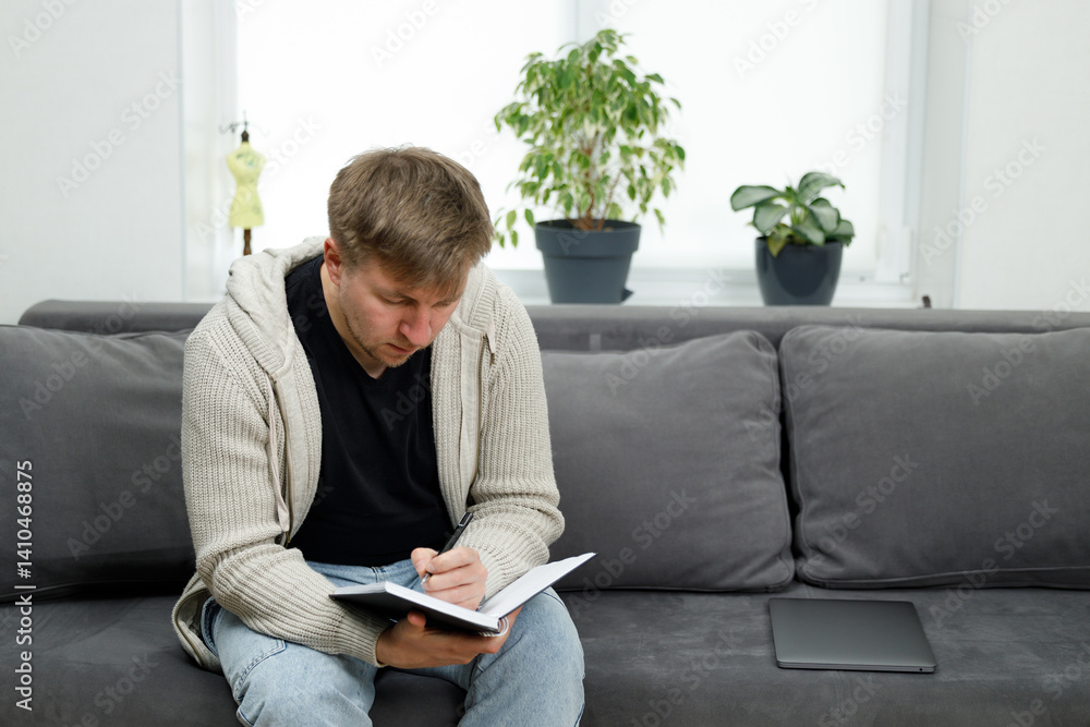 Man Sitting on Couch Writing in Notebook in a Creative Environment Man Sitting on Couch Writing in Notebook in a Creative Environment