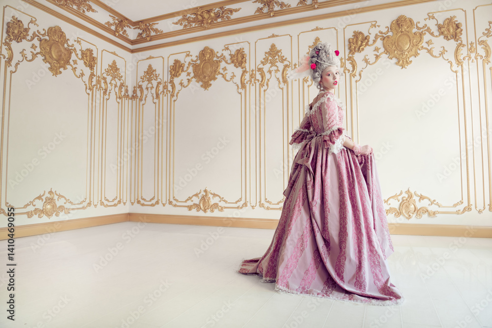 Fototapeta premium Elegant woman in a flowing pink gown standing in a lavishly decorated room with ornate gold details