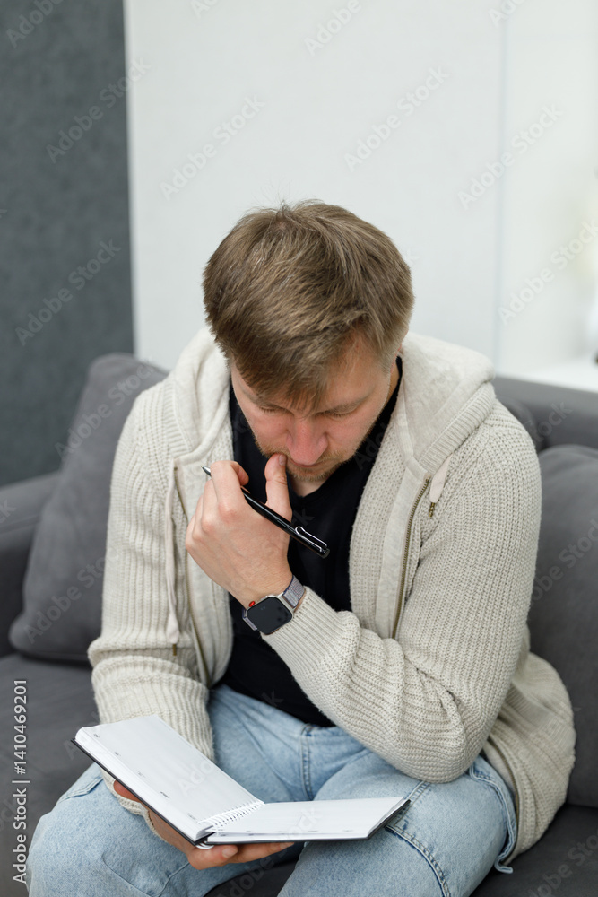 Fototapeta premium Man Sitting on Couch Writing in Notebook in a Creative Environment