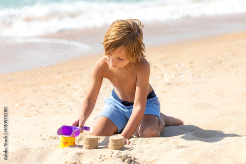 Obraz na płótnie Happy child little boy playing with the sand on the beach, building sand castle, enjoying summer, playing. Advertising for tour operators, hotels, airlines. Vacation concept. w salonie
