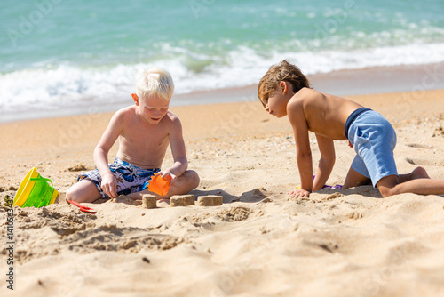 Obraz na płótnie Children two little boys playing on the beach on summer holidays. Children having fun with a sand on the seashore. Vacation concept. Happy sunny day. Joyful children with beautiful sea, sand w salonie
