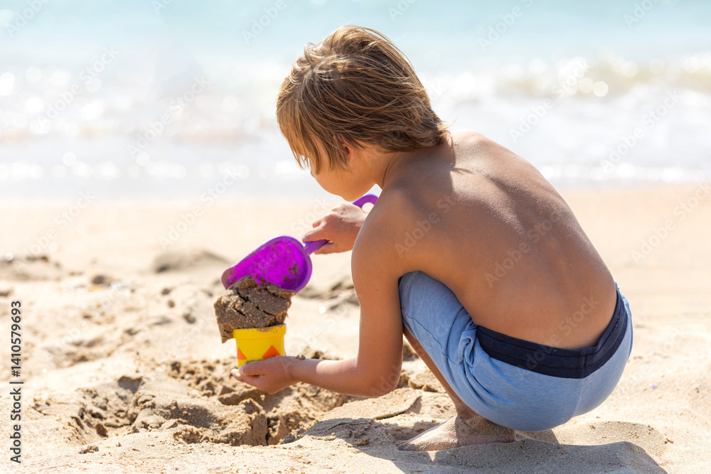 Side view child little boy playing with the sand on the beach, building sand castle, enjoying summer, playing. Advertising for tour operators, hotels, airlines. Vacation concept.