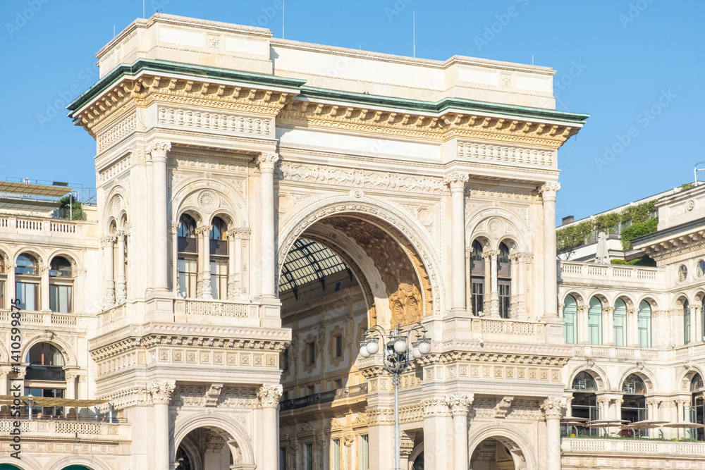Obraz premium Main entrance arch of the Galleria Vittorio Emanuele on Cathedral square in sunny day, Milan, Lombardy, Italy. Neoclassical archway with ornate columns on Piazza del Duomo