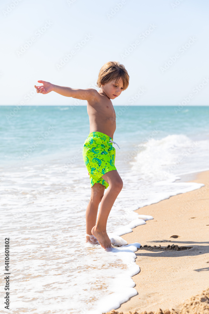 Cute little boy playing on the beach on summer vacation. Joyful child in nature with beautiful sea and sand background. Happy kid on vacation, walking on the beach and having fun. Freedom concept
