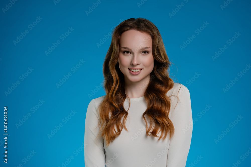 Woman with long hair poses in studio against a vibrant blue background, expressing a warm and inviting emotion Woman with long hair poses in studio against a vibrant blue background, expressing a warm and inviting emotion