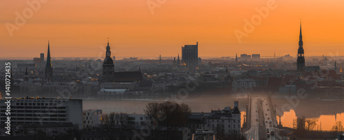 Obraz na płótnie A warm sunrise illuminates Riga's old town, featuring St. Peter's Church, Riga Cathedral, a bridge over the Daugava River, and light morning mist. w salonie