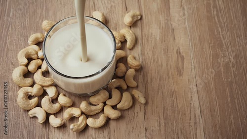 A glass of cashew milk surrounded by raw cashews on a wooden surface.