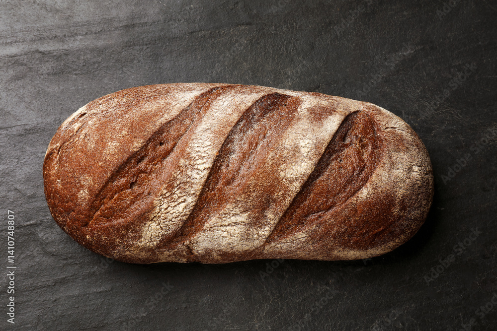 Fresh loaf of bread on black table, top view