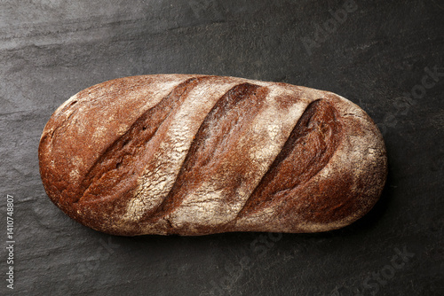Fresh loaf of bread on black table, top view