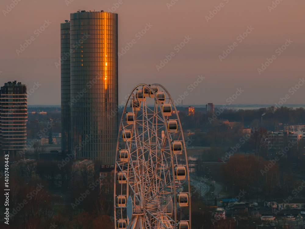 Serene sunrise over Riga, Latvia, featuring the Swedbank headquarters with its glass facade reflecting golden light and a Ferris wheel in the foreground.