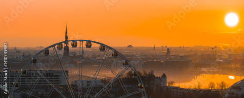 Obraz na płótnie A warm sunrise illuminates Riga, Latvia, with a Ferris wheel in the foreground, St. Peter's Church spire, historic buildings, and the Daugava River. w salonie