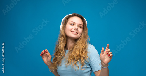 Obraz na płótnie Cheerful young woman wearing blue t-shirt listening to music with headphones, dancing isolated over blue background. w salonie