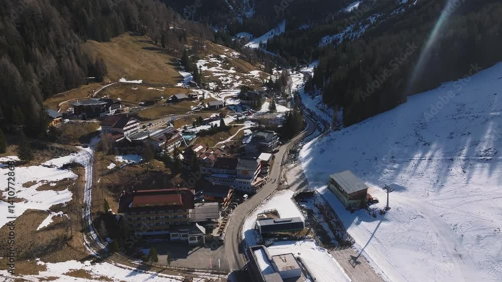 Aerial view of a luxury hotel in the Dolomites, surrounded by snow dusted slopes, forests, grassy areas, and winding roads. Camera pans smoothly. Aerial view of a luxury hotel in the Dolomites, surrounded by snow dusted slopes, forests, grassy areas, and winding roads. Camera pans smoothly.