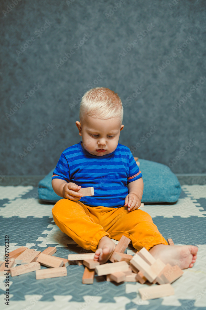 Toddler boy in a T-shirt and pants playing with toys at home. Children's home clothes. Child's self-development at home.