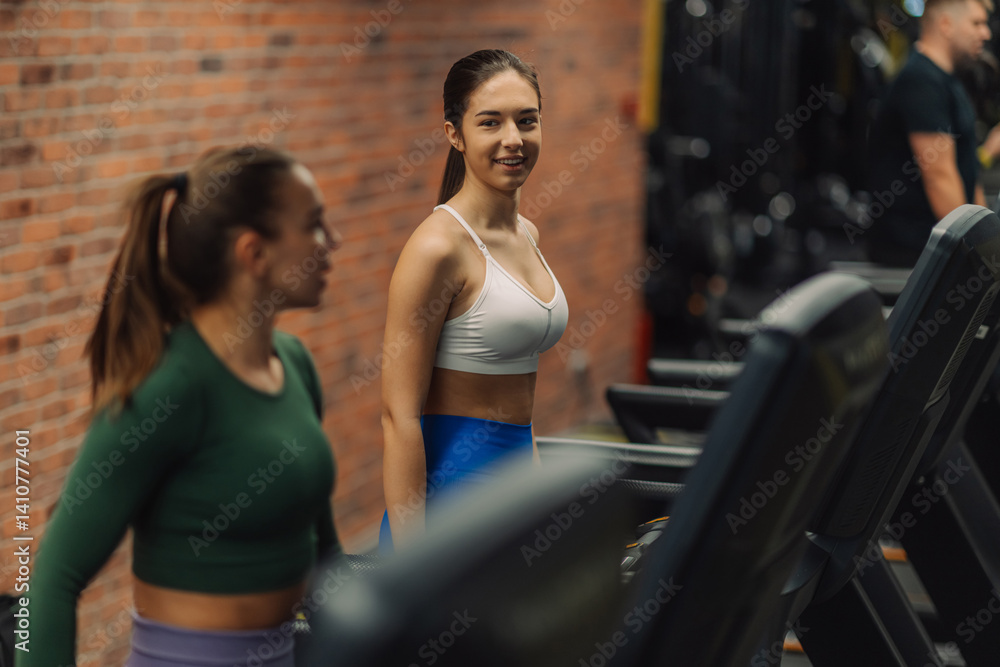 Fototapeta premium Two young women exercising on treadmills in modern gym