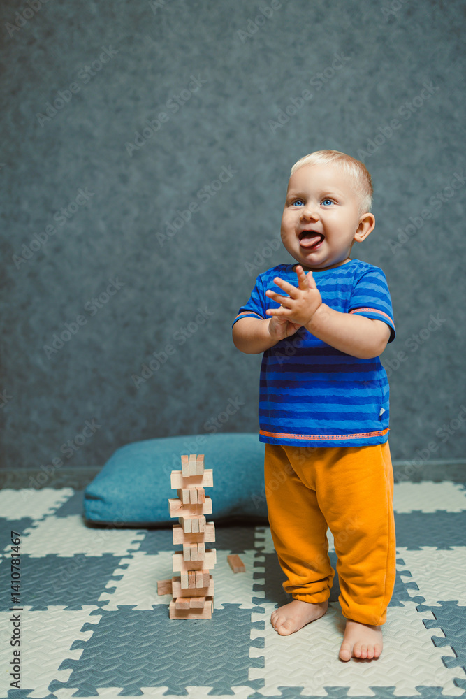 Toddler boy in a T-shirt and pants playing with toys at home. Children's home clothes. Child's self-development at home.