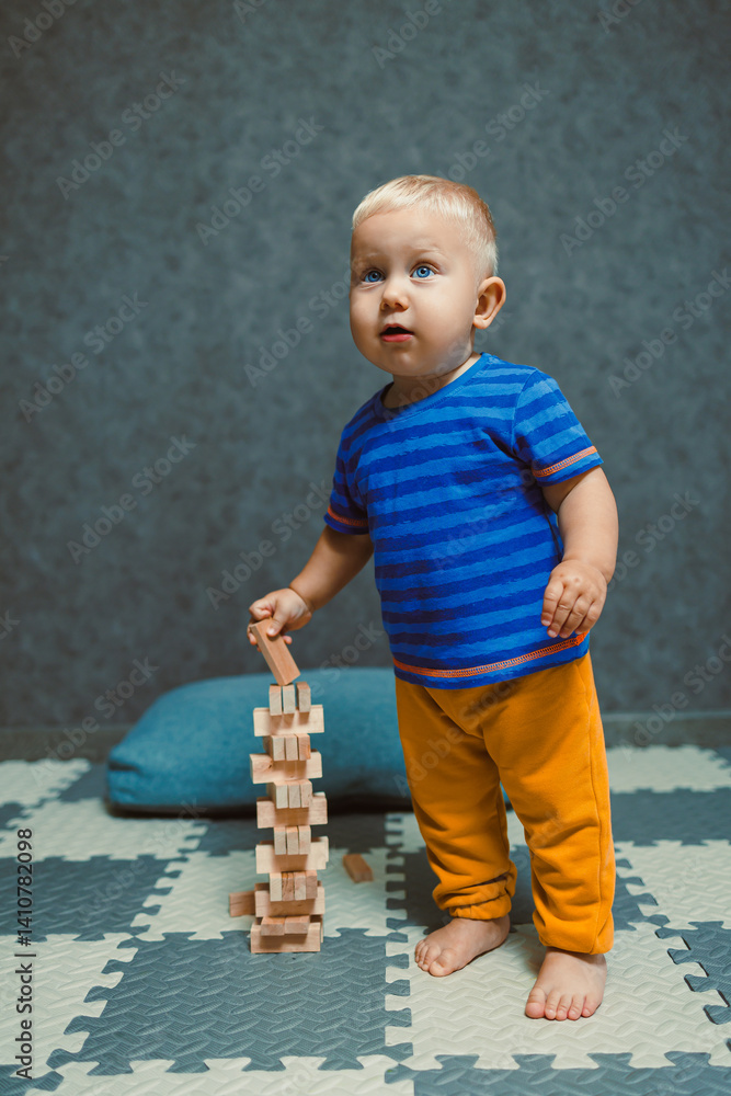 One-year-old boy running around the nursery at home. Toddler boy in a T-shirt and pants playing with toys at home. Children's home clothes. Child's self-development at home.