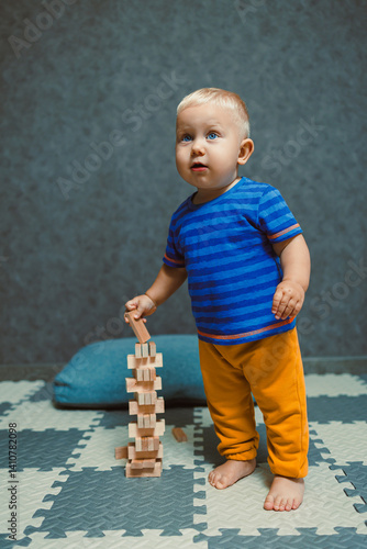 Obraz na płótnie One-year-old boy running around the nursery at home. Toddler boy in a T-shirt and pants playing with toys at home. Children's home clothes. Child's self-development at home. w salonie