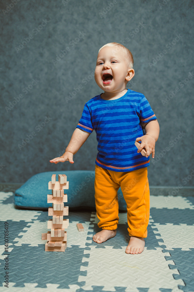 A one-year-old boy at home in a t-shirt and pants is playing in the room. The child is having fun playing on his own.