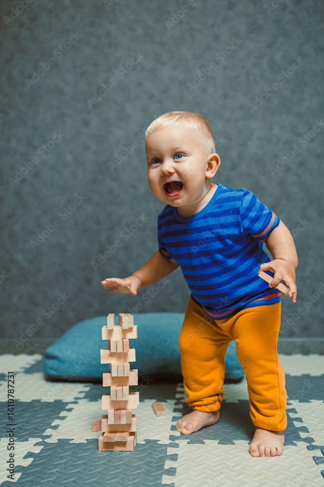 A one-year-old boy at home in a t-shirt and pants is playing in the room. The child is having fun playing on his own.