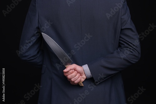 Businessman holding knife behind his back on black background, closeup