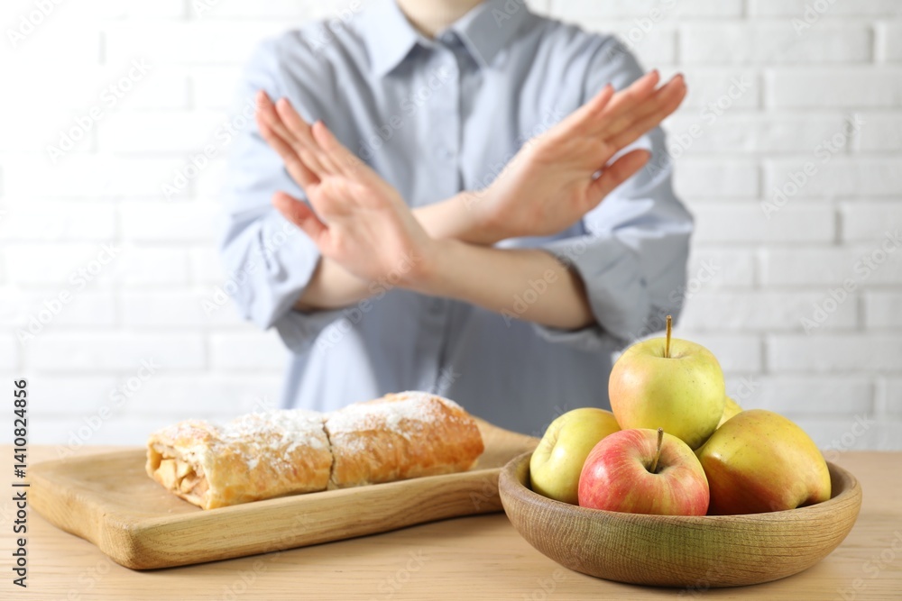 Woman refusing to eat products at wooden table near white brick wall, selective focus. Food allergy concept Woman refusing to eat products at wooden table near white brick wall, selective focus. Food allergy concept