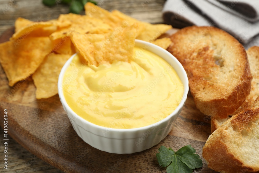 Tasty cheese dipping sauce in bowl, nacho chips and croutons on table, closeup Tasty cheese dipping sauce in bowl, nacho chips and croutons on table, closeup