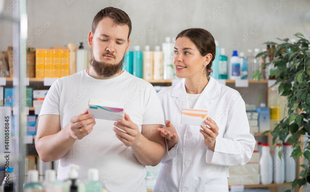 Obraz premium Young man buyer choosing box of pills with help of young woman pharmacist in pharmacy