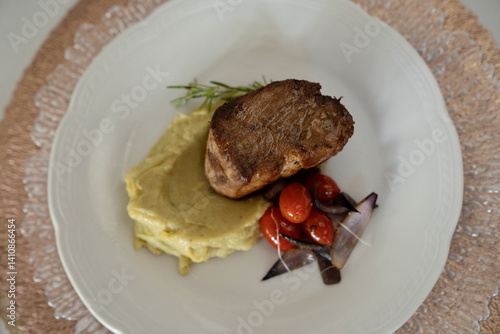 Gourmet main course. Top view of a roasted pork loin with mashed sweet potatoes and cherry tomatoes, in a white dish