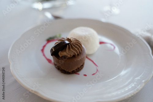 Gourmet menu in a social event. Desserts. Closeup view of a chocolate marquise with ice cream in a white dish. Beautiful silverware and table arrangement