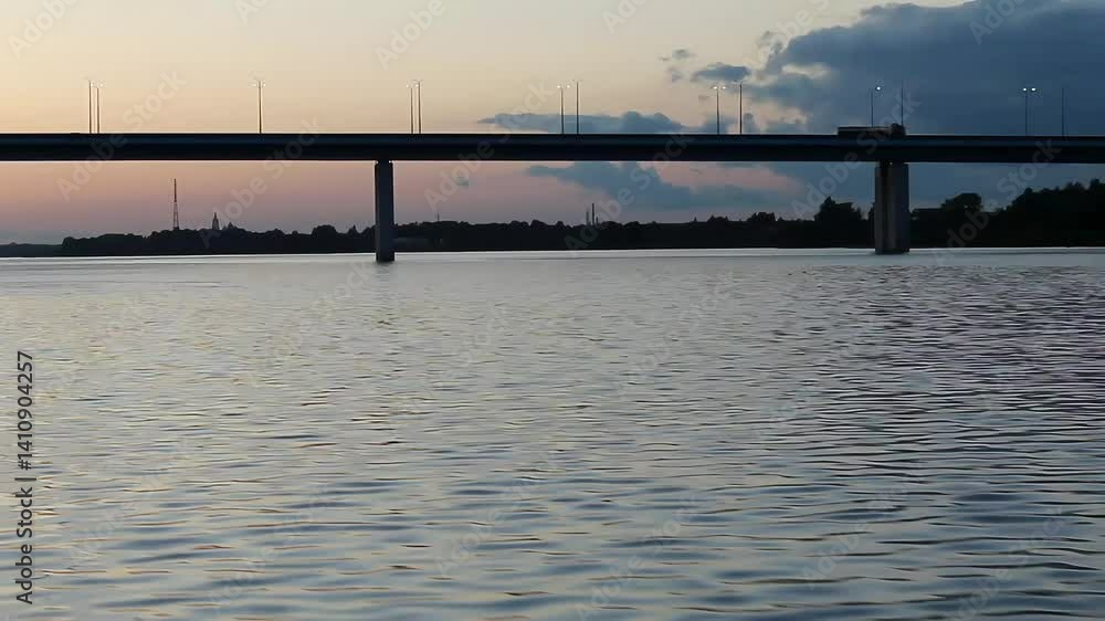Sunset view of highway bridge over calm river with truck silhouette against pastel sky. Concept of transportation infrastructure, urban landscape environment. Sunset view of highway bridge over calm river with truck silhouette against pastel sky. Concept of transportation infrastructure, urban landscape environment.