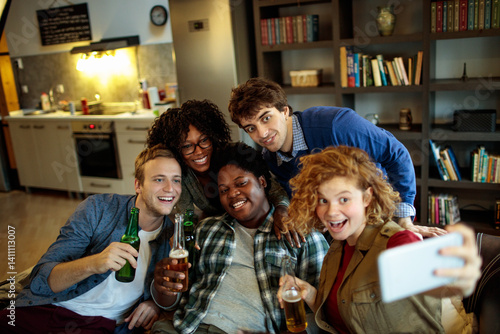 Obraz na płótnie Young and diverse group of friends having a get together and taking selfies on a smartphone on the couch in the living room w salonie