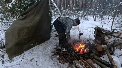 survivalist adds wood to a fire in a frosty winter forest