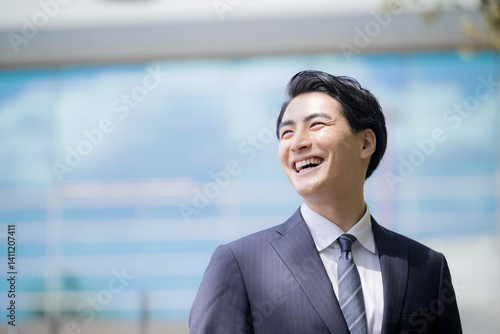 Fotografía 青空の都会ビル前で笑顔で未来や目標を見上げる若い男性のサラリーマンクローズアップ