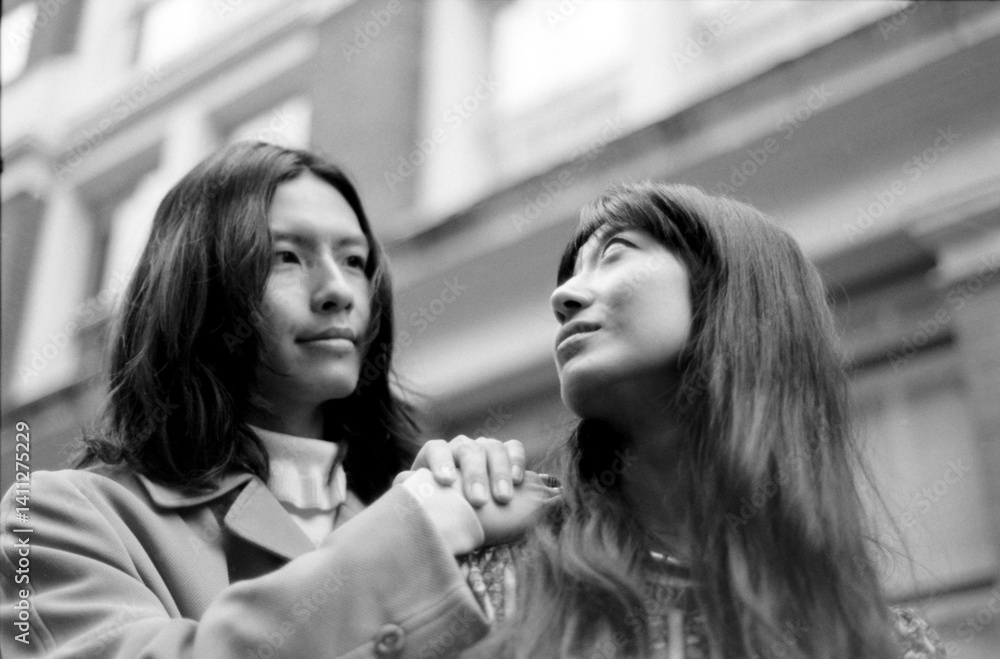 Fototapeta premium Young couple holding hands and looking up in urban setting, grainy monochrome film aesthetic