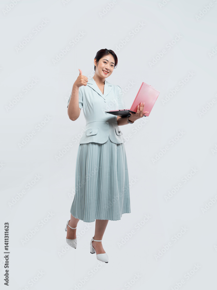 Smiling woman in light blue dress holding laptop and giving thumbs up gesture of approval Smiling woman in light blue dress holding laptop and giving thumbs up gesture of approval